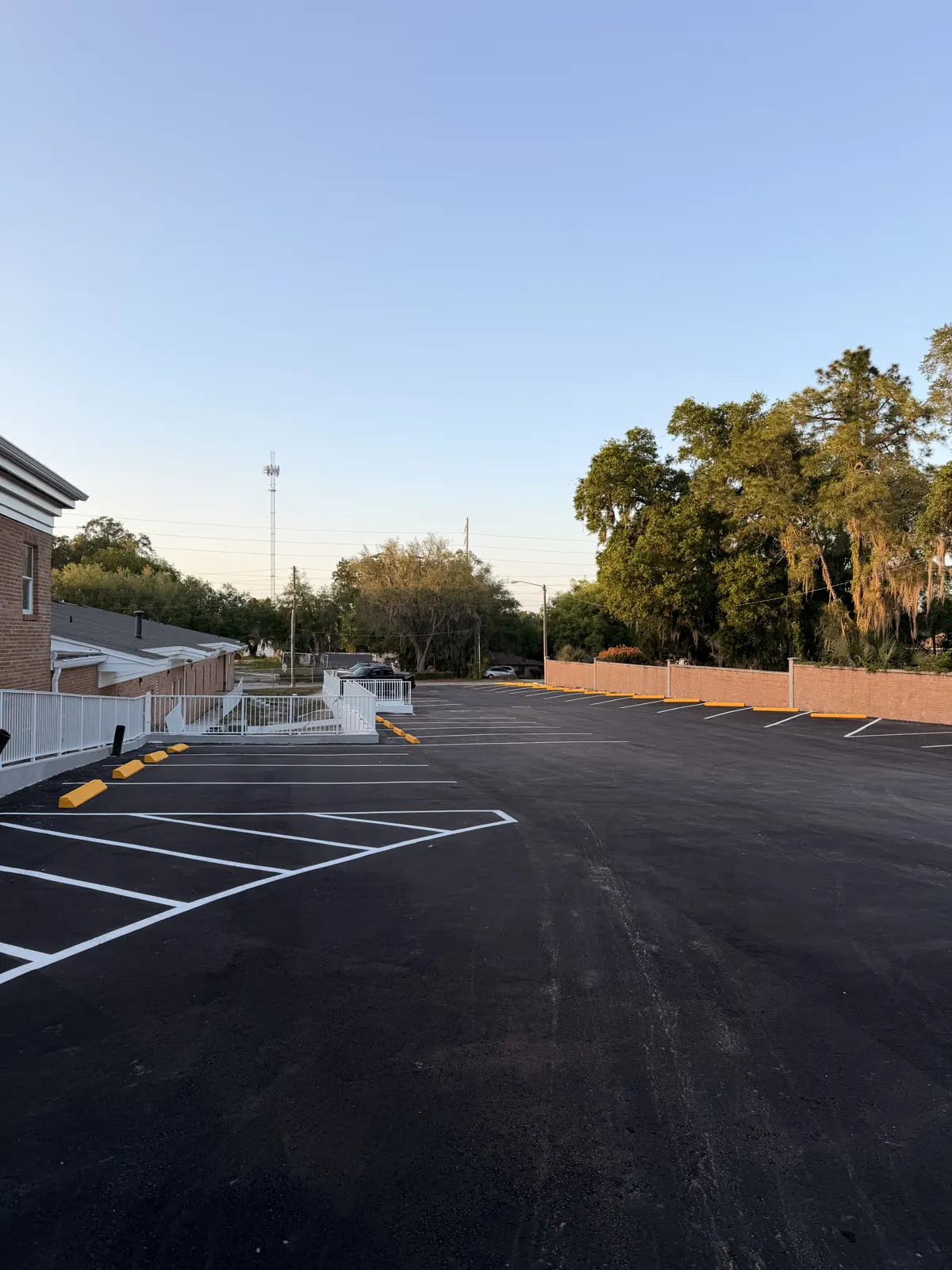 New asphalt parking lot with white stall lines and yellow curb paint beside a building