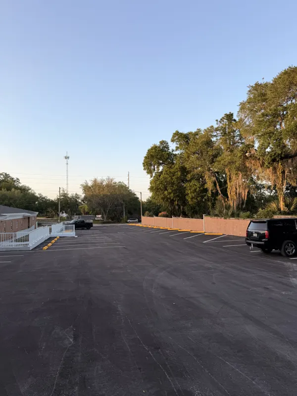 Wide view of a newly paved and striped parking lot with mature oaks along the edge